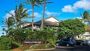A hotel with a sign reading "Regency at Poipu Kai," surrounded by lush greenery and palm trees.