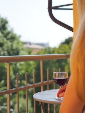 Eine Person hält ein Weinglas auf einem Balkon mit Geländer.