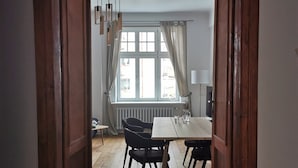 An open doorway leading to a dining area with a table and chairs, a window with curtains, and a radiator. - Designer Apartment 110m² w/ King Beds, Balcony, Smart TV + Equipped Kitchen (Kraków)