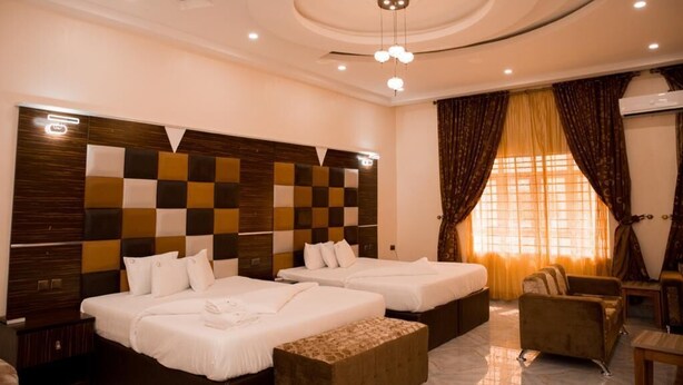 Habitación de hotel con dos camas, cabecera de madera, un sofá y un ventanal con cortinas.