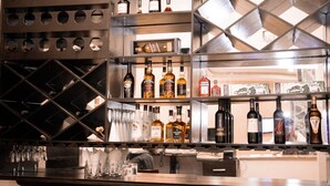 Zona de bar con múltiples estanterías que exhiben diferentes botellas de licor, vasos y una botellera.