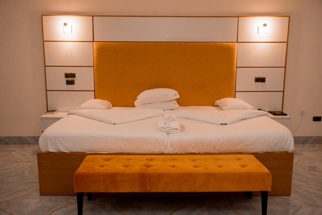 A modern bedroom with a large bed, two bedside tables, a bench, and wall-mounted lighting.