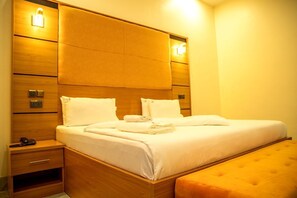 Ein Hotelzimmer mit einem hölzernen Kopfteil, einem Nachttisch mit Telefon und passendem Hocker.
