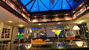 Zona de bar con techo de vidrio, estantes llenos de botellas de licor y diferentes vasos sobre el mostrador.