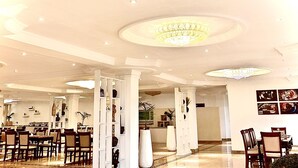 Un vestíbulo amplio con techos altos, candelabros y una zona de estar con mesas y sillas.