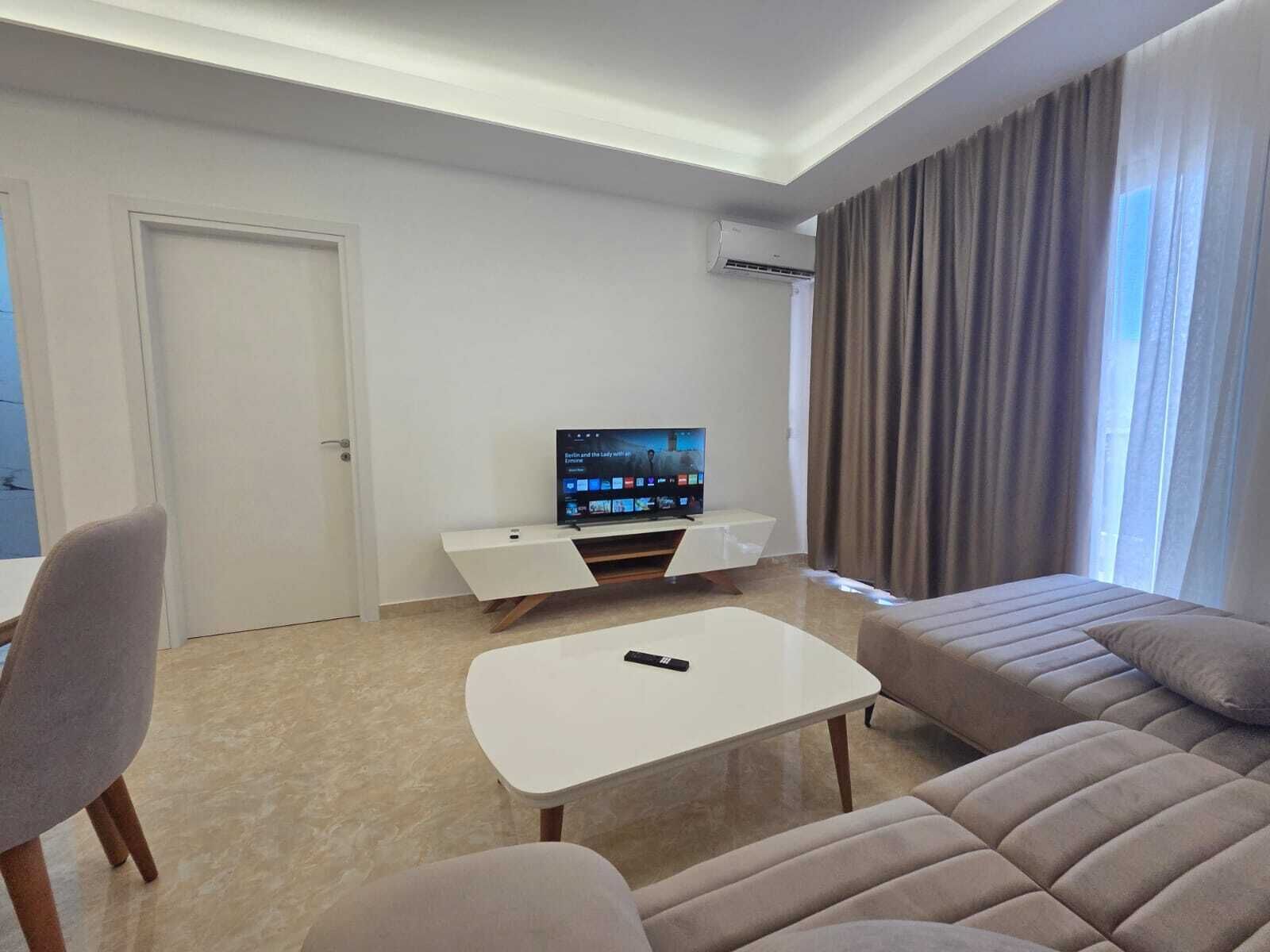 A modern living room with a sofa, a coffee table, a TV on a stand, and a door.