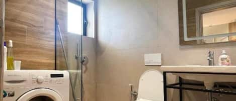 Casa de banho compacta com máquina de lavar roupa, sanita e lavatório com espelho em cima.