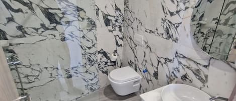 Un baño con pared de mármol, inodoro y lavabo.