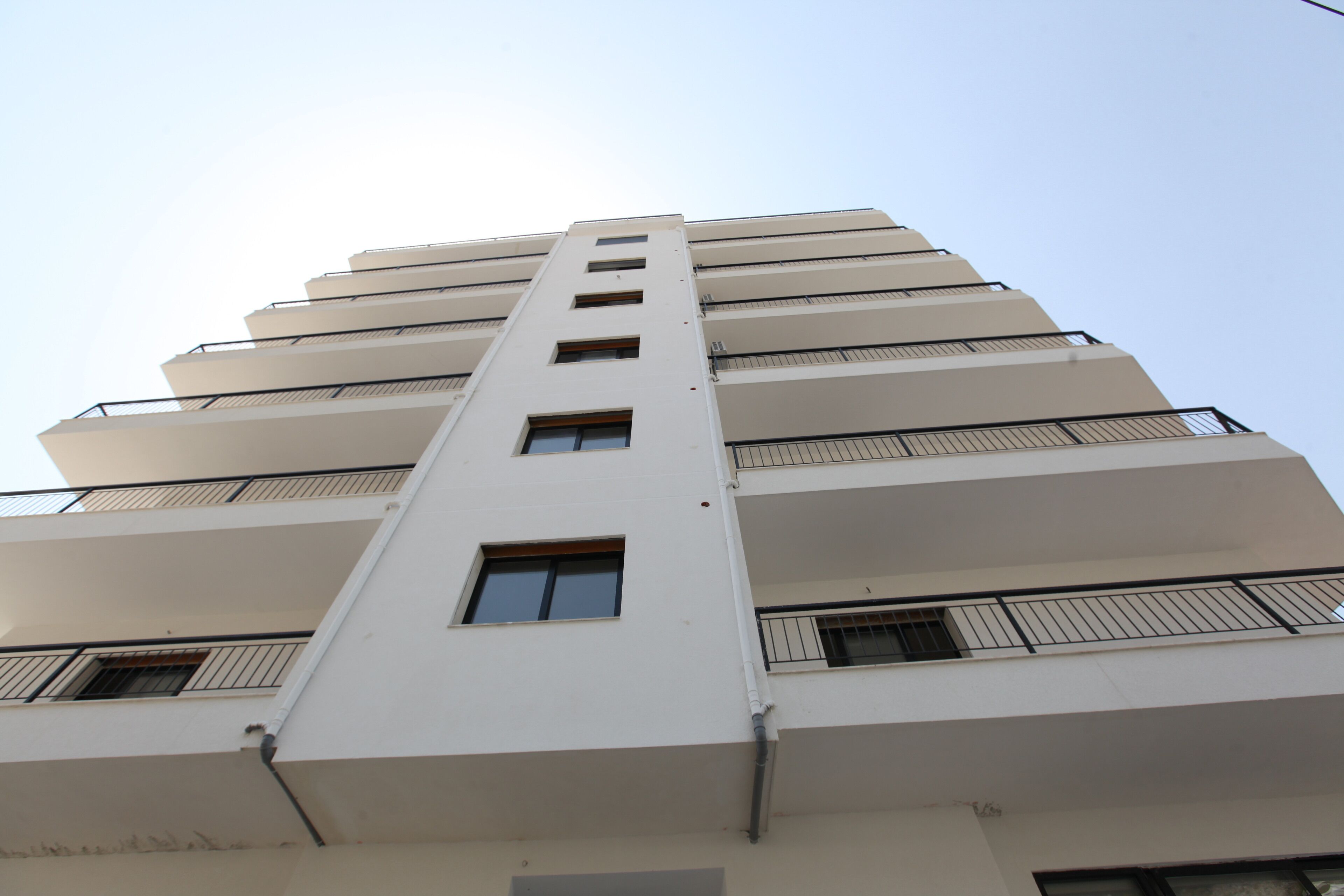 A multi-story building with a central vertical corridor, balconies on each floor, and a clear sky in the background.