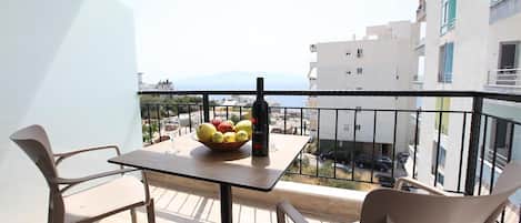 A balcony with a table, chairs, a bottle, and a bowl of fruit.