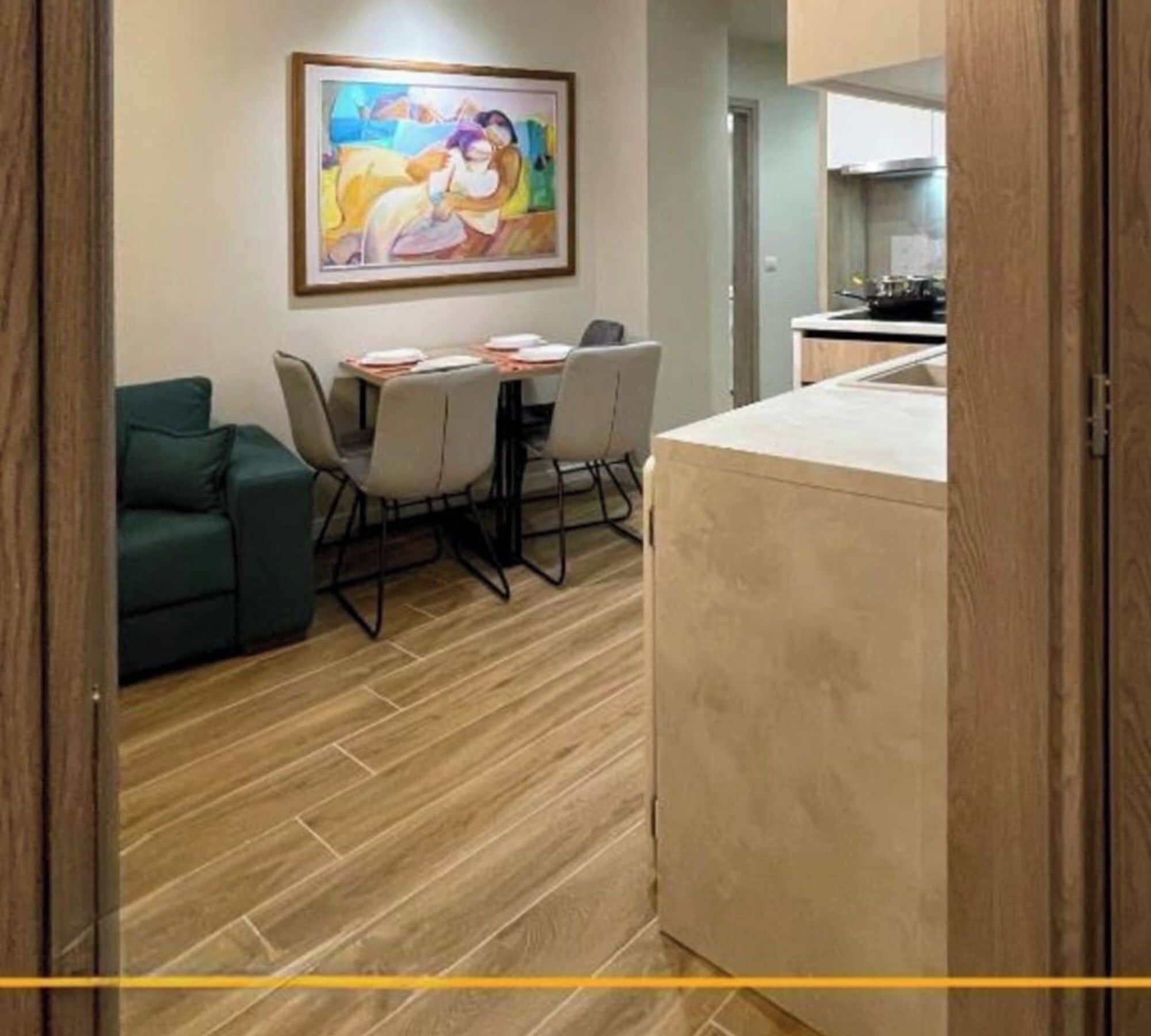 Un coin repas avec une table et des chaises, un tableau accroché au mur et une cuisine en arrière-plan.