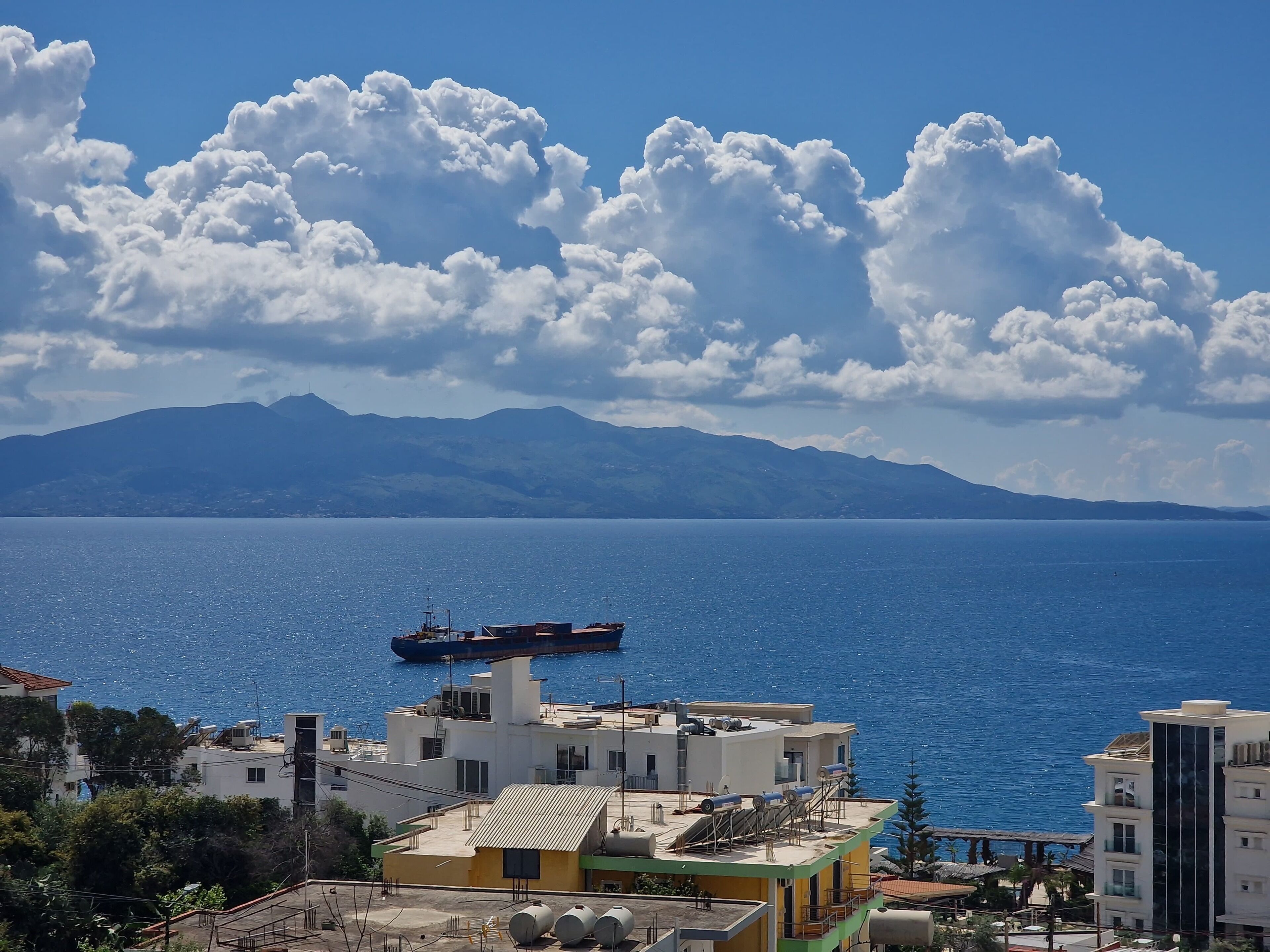 A coastal view with a large body of water, a ship, and buildings with balconies and solar panels.