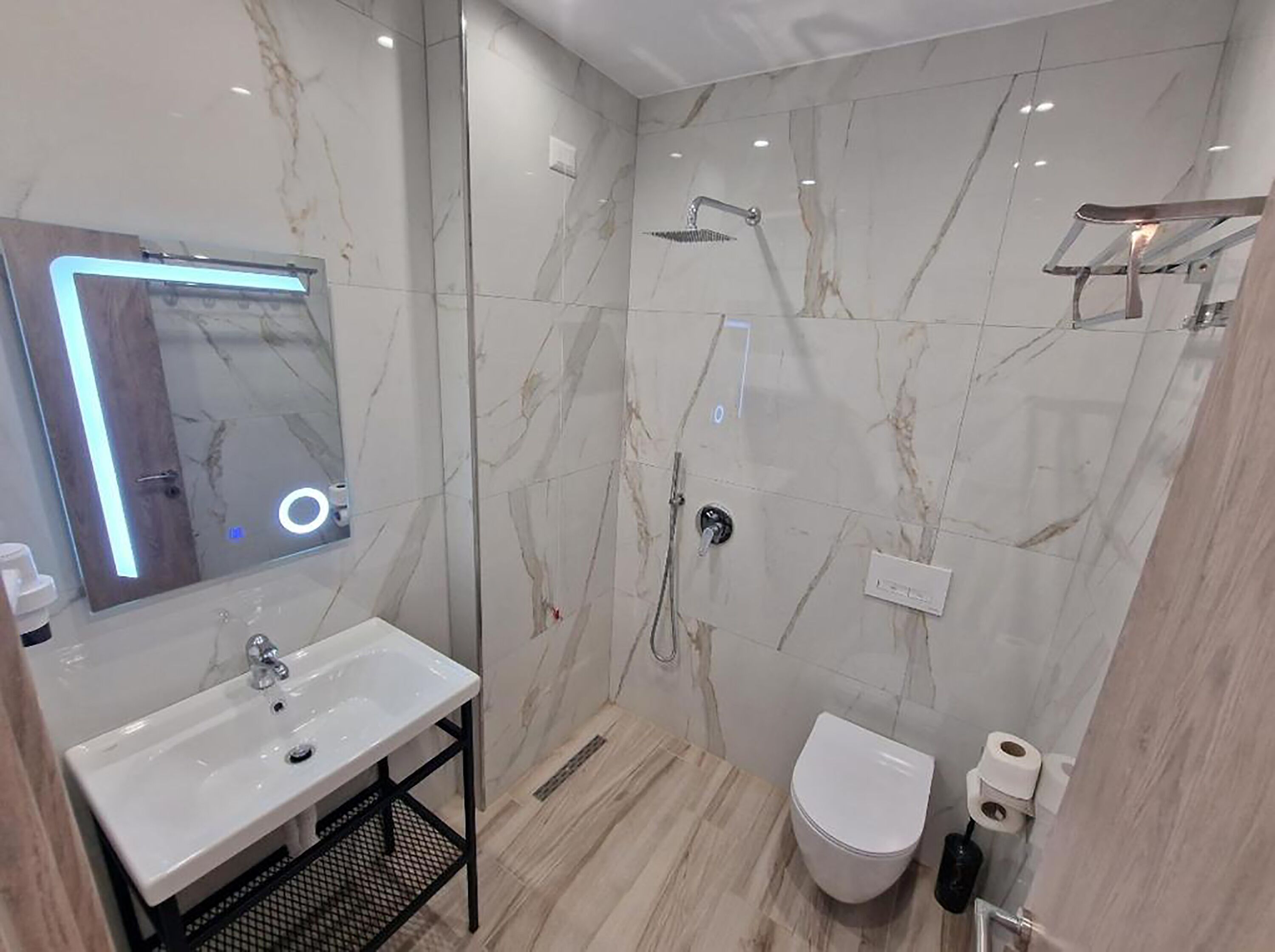 A modern bathroom with a marble wall, a sink with a mirror, a shower, and a toilet.