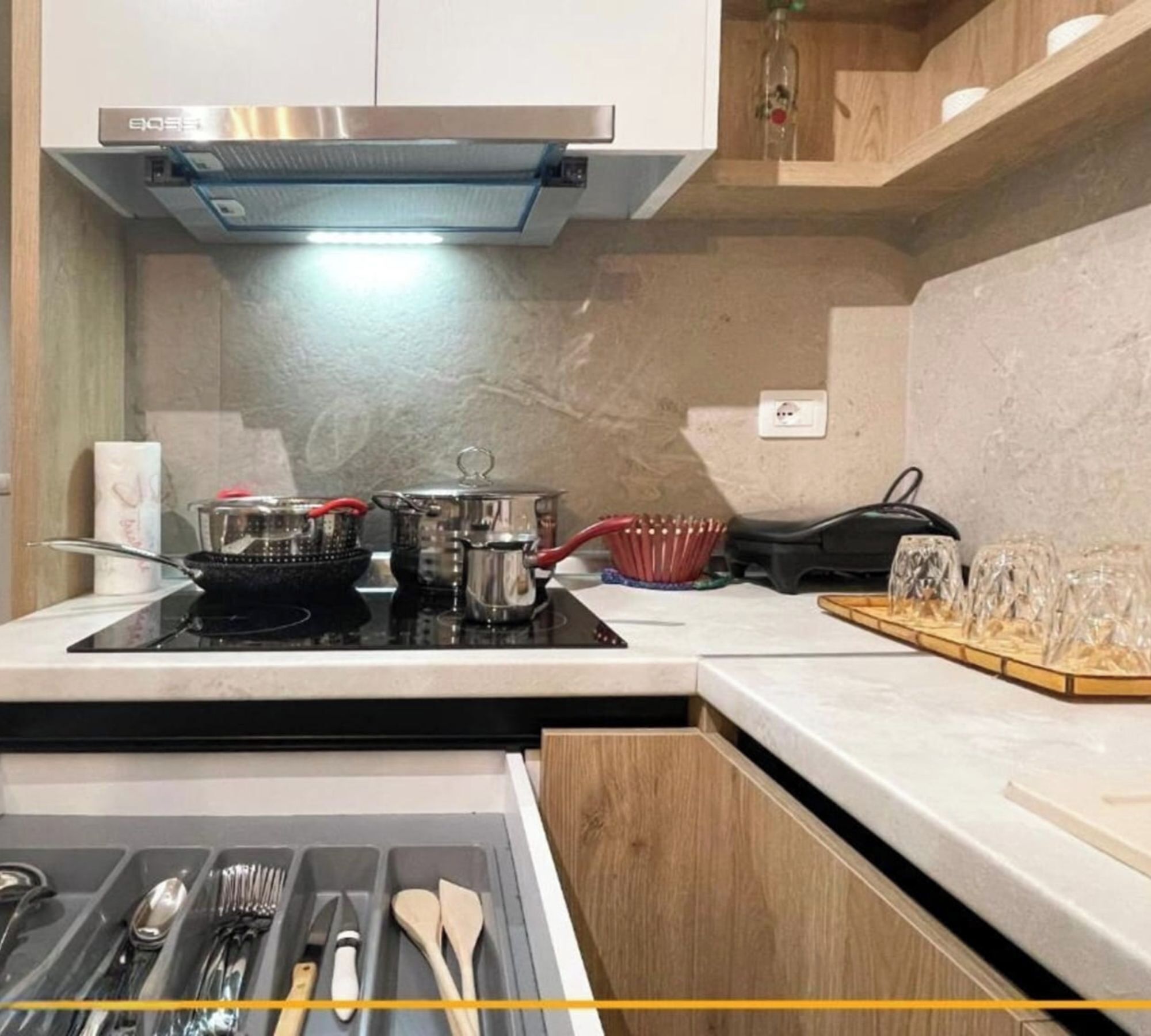 Una cocina con estufa, ollas, tetera y microondas. Hay un estante de madera sobre la estufa y una encimera con un bloque de cuchillos.