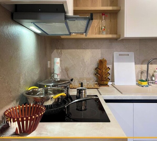 A modern kitchen with a stove, pots, a colander, and a wooden utensil holder. - Joanna Suites (Sarandë)