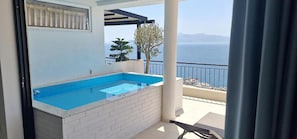 Un balcón con piscina, vista al mar y un árbol.