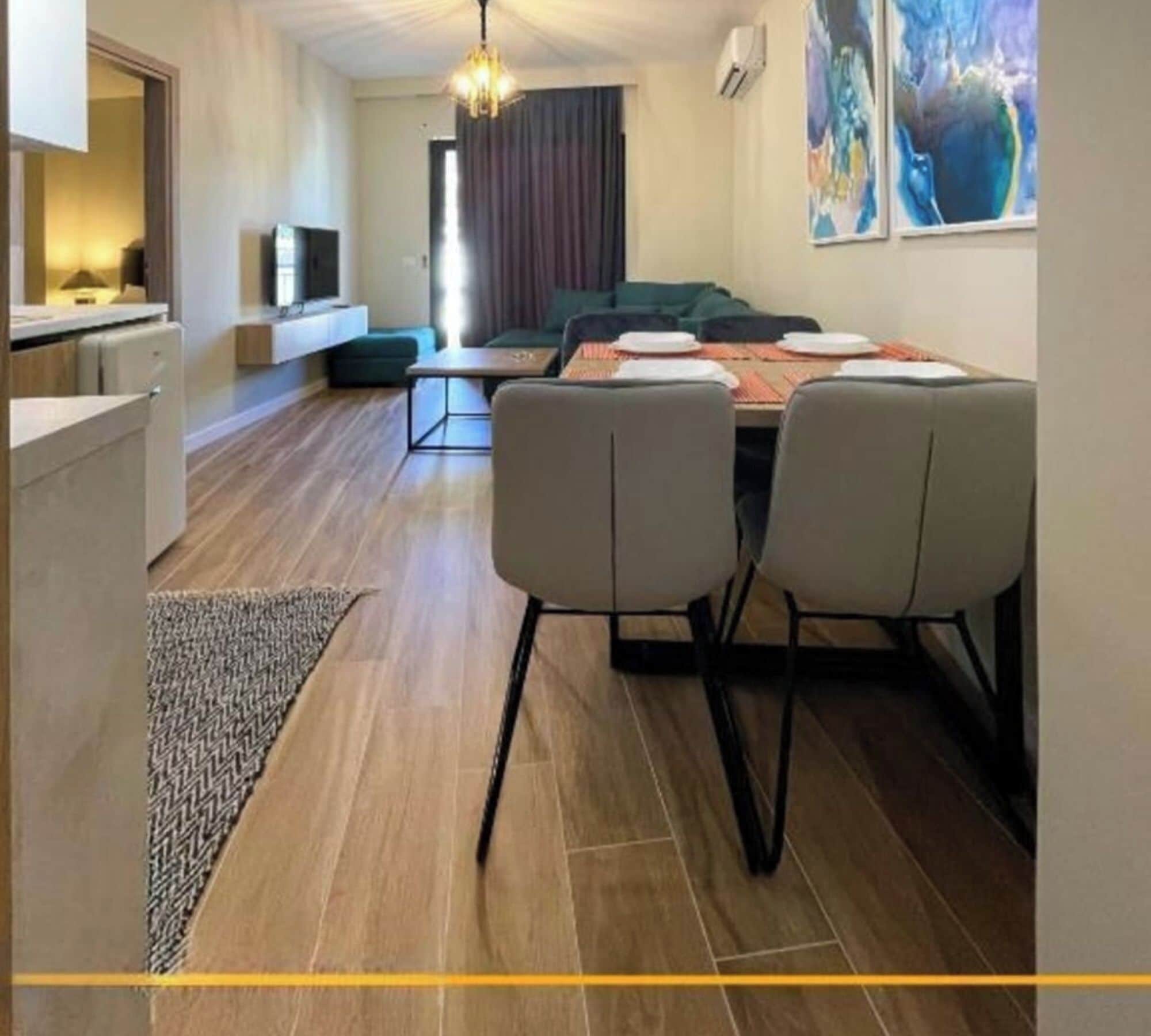 Una cocina moderna con horno y microondas integrados, un comedor con mesa y sillas, y una sala de estar con sofá y televisor.