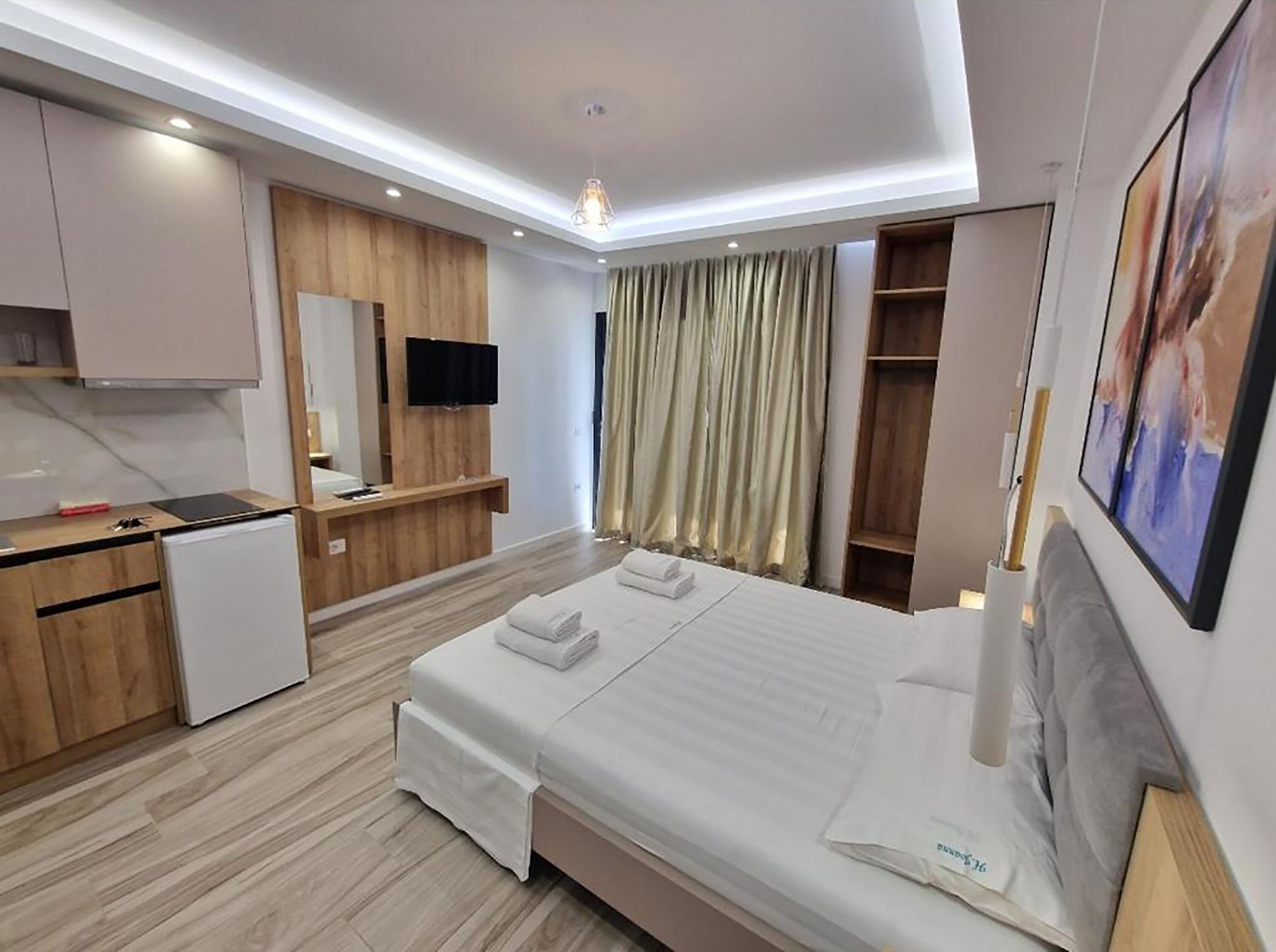 A modern hotel room with a bed, a desk, a television, and a wardrobe.