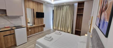 A modern hotel room with a bed, a desk, a television, and a wardrobe.