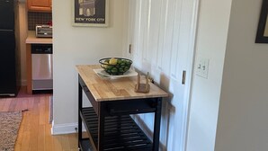 A kitchen with wooden cabinets, a black refrigerator, a dishwasher, a wooden table with a bowl of fruit, and a framed picture on the wall. - Calm Relaxing Home Away from Home   (Westfield)