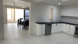 A modern kitchen with white cabinets, a black countertop, and a dishwasher. There is a dining area with a table and chairs visible through an open doorway.