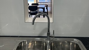 A modern kitchen with a stainless steel sink, a black marble countertop, and a view of a dining area with a table and chairs through a glass door.