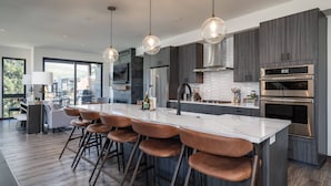A modern kitchen with a large island, bar stools, stainless steel appliances, and a view of the outdoors.