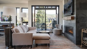 A modern living room with a sectional sofa, a fireplace, and a large window offering a view of trees and buildings.