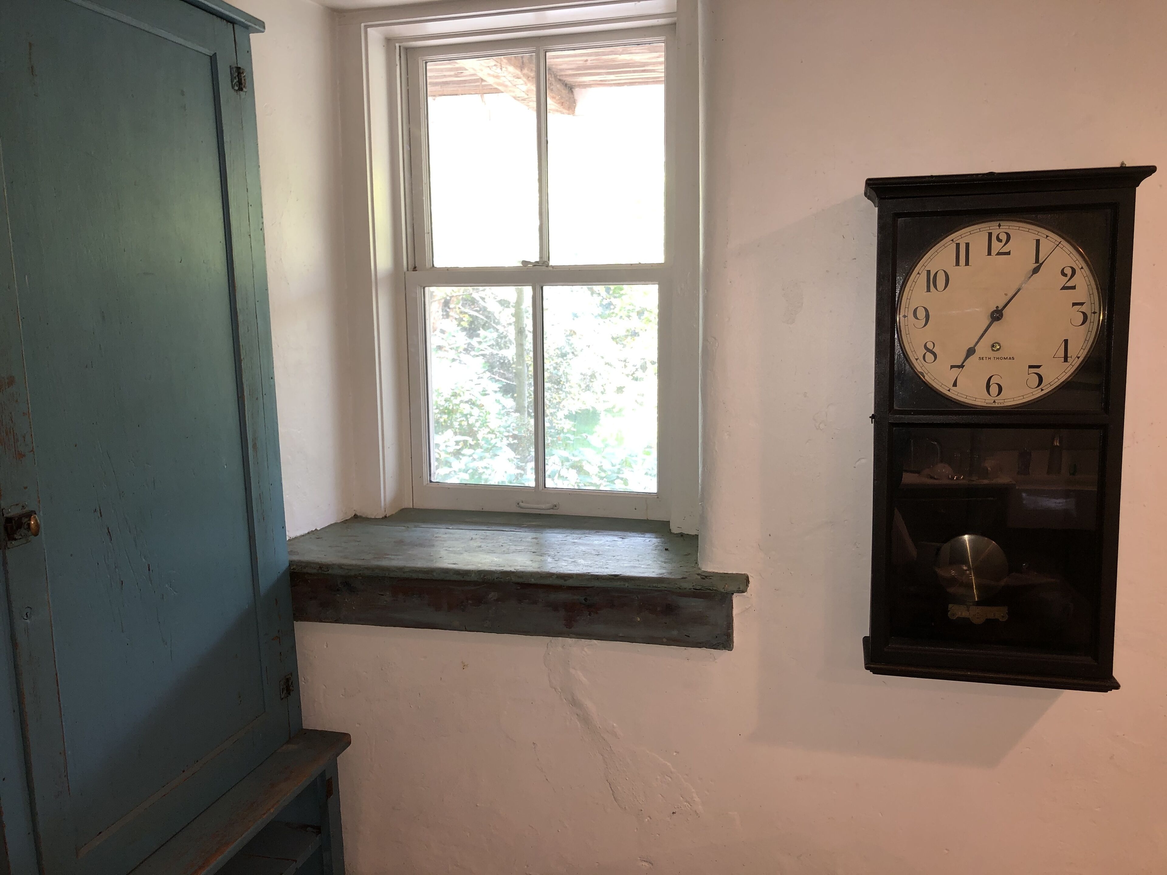 Une pièce avec une fenêtre, une horloge et une porte bleue.