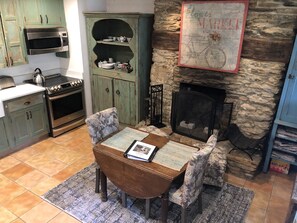 A cozy kitchen with a stone fireplace, a dining table with chairs, and a microwave above the cabinets.