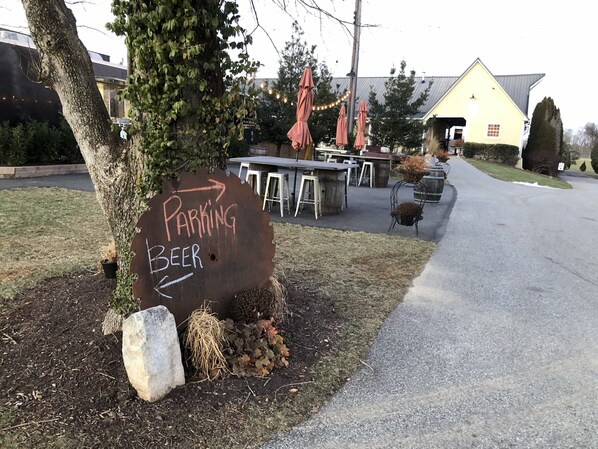 A rustic wooden sign with 'PARKING' and 'BEER' written on it, placed near a building with outdoor seating and string lights.