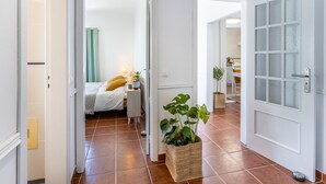 A hallway with a bed, a bedside table with a lamp, and a potted plant.