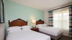 Una habitación de hotel con dos camas individuales, una mesita de noche con lámpara y una ventana con cortinas a rayas.