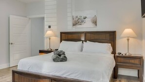 A neatly made bed with white linens, two bedside tables with lamps, a door to the left, and a painting above the bed. - Modern and Comfortable Home Close to Downtown (Dallas)