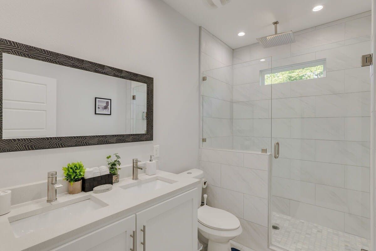 A modern bathroom with a large mirror, white tiles, a shower, and a toilet.