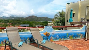 A terrace with two lounge chairs, a mural of an underwater scene, and a view of the landscape.