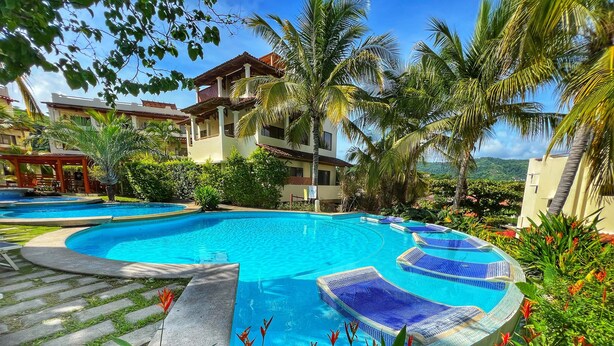 A pool area with clear blue water, lounge chairs, and tropical plants.