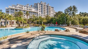 Un hotel con un amplio espacio de piscina, que incluye un jacuzzi, rodeado de palmeras y sillones de descanso.