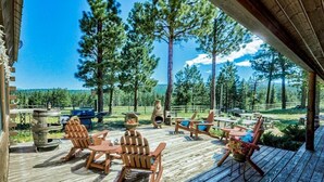 A wooden deck with outdoor furniture, a fire pit, and a view of a forest. - TrailsEndRanch ⛰Views, HotTub, Horseback riding on 1000's ac (Angel Fire)