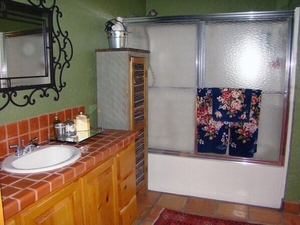A bathroom with a sink, wooden cabinets, a mirror, a shower with a glass door, and a floral towel hanging on the shower door.