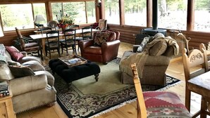 A cozy cabin interior with a wooden ceiling, large windows, a dining area with a table and chairs, and a fireplace. - TrailsEndRanch ⛰Views, HotTub, Horseback riding on 1000's ac (Angel Fire)