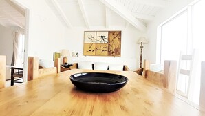 A spacious dining area with a wooden table, a black bowl in the center, and a large window providing natural light.