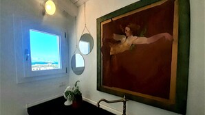 A bathroom with a large window, a sink, and a painting on the wall.