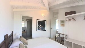 A bedroom with a large bed, a wardrobe, a framed picture on the wall, and a door leading to another room.