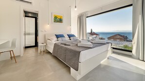 A modern bedroom with a large bed, a desk, and a view of the sea.