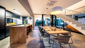 A modern kitchen with a central island, dining area with wicker chairs, and a staircase leading to an outdoor area.