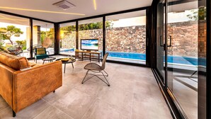 A modern living room with a large window, a sofa, a dining table, and a TV.