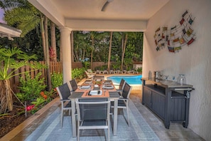 Un área de comedor al aire libre con piscina, rodeada de plantas tropicales y una valla de madera.