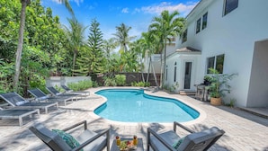 A swimming pool with lounge chairs and a table with fruit and drinks.