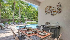 An outdoor dining area with a pool, lounge chairs, and a barbecue grill.
